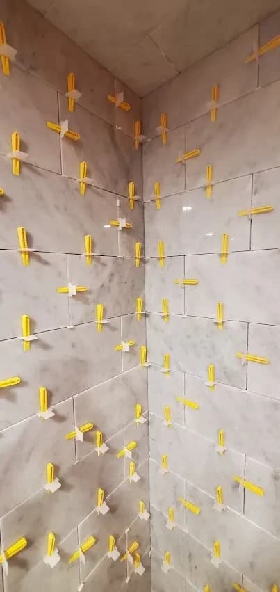 Shower walls being tiled, with levelling clips in every joint