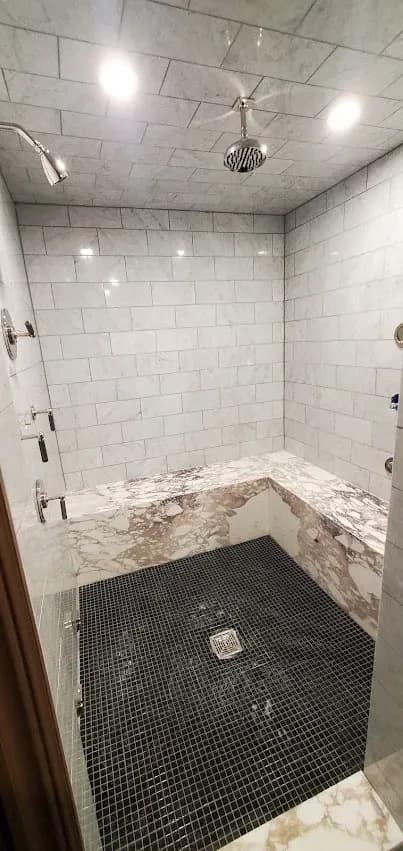 The finished shower: marble walls and bench, black mosaic floor, rain head