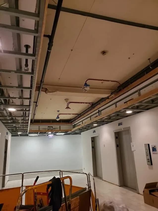 A lobby ceiling being framed around sprinkler lines by the elevators