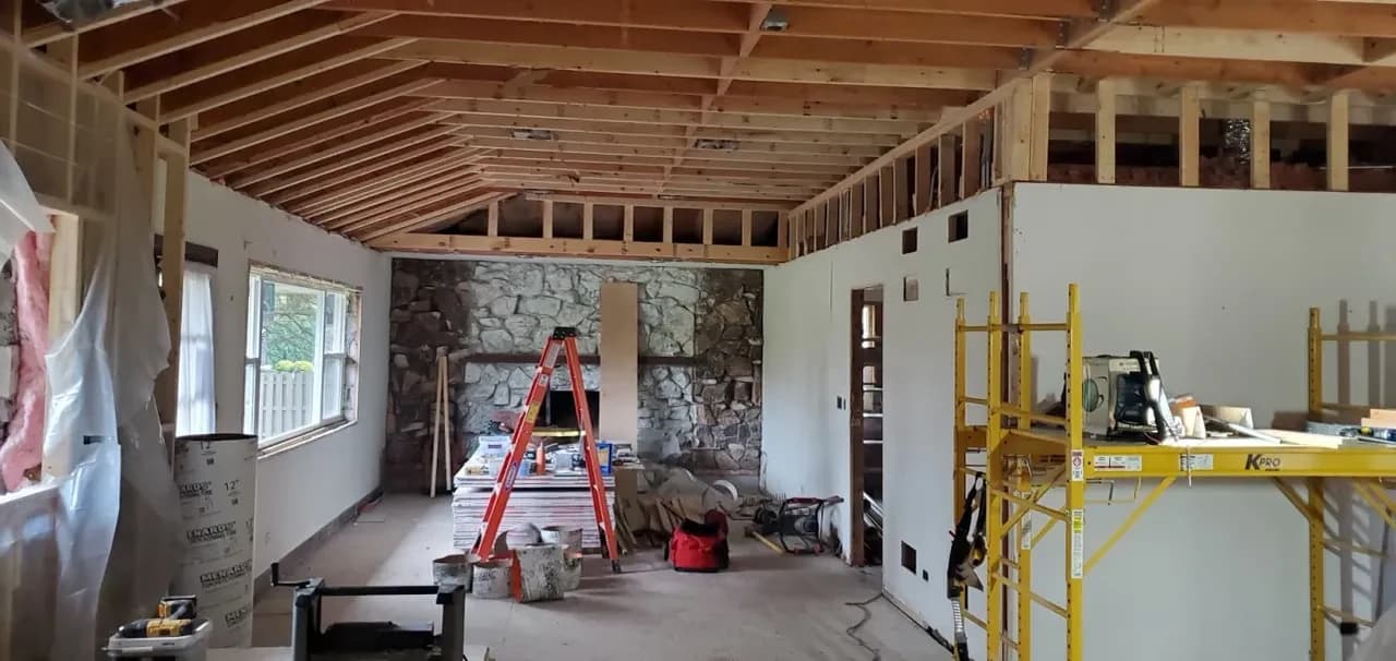 A house being opened up: exposed rafters, a stone fireplace, a ladder and scaffolding mid-renovation